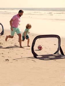 un papa et son enfant jouant au foot avec les cages de foot pop up sur la plage